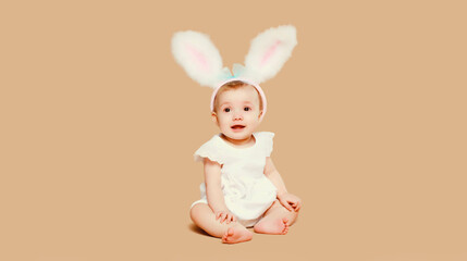 Portrait cute baby with easter rabbit ears sitting on brown studio background