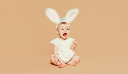 Portrait cute baby with easter rabbit ears sitting on brown studio background
