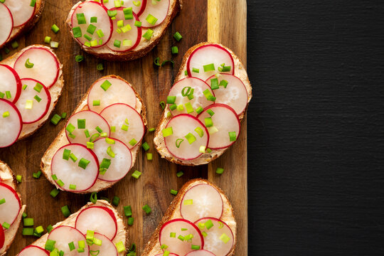 Homemade Lemon Radish Tartine on a wooden board on a black background, top view. Copy space.