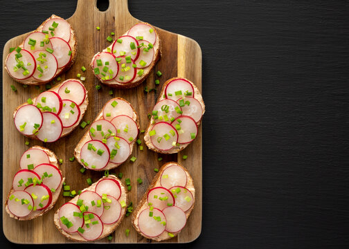 Homemade Lemon Radish Tartine on a wooden board on a black background, top view. Copy space.