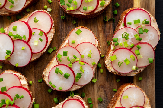 Homemade Lemon Radish Tartine on a wooden board on a black background, top view. Close-up.