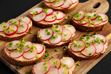 Homemade Lemon Radish Tartine on a wooden board on a black background, side view.