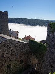 Vista de nubes blancas bajas entre las torres, con la montaña verde al fondo desde el Castillo de Castro Caldelas en Orense, pueblo bonito de España en verano de 2021