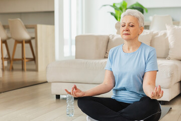 Yoga mindfulness meditation. Senior adult mature woman practicing yoga at home. Mid age old lady sitting in lotus pose on yoga mat meditating relaxing. Older middle aged woman doing breathing practice