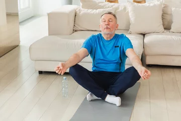 Foto op Canvas Yoga mindfulness meditation. Senior adult mature man practicing yoga at home. Mid age old grandfather sitting in lotus pose on yoga mat meditating relaxing. Older man doing breathing practice © Юлия Завалишина