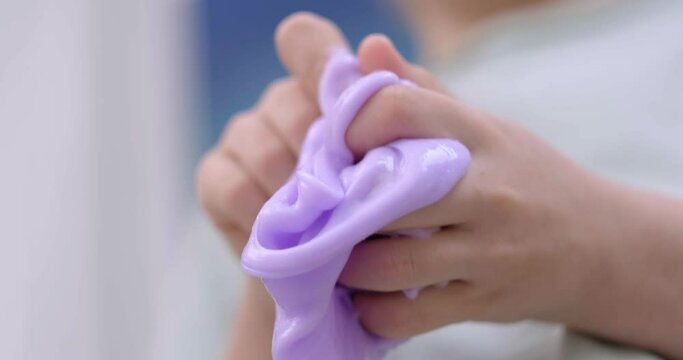 Child delightfully playing with homemade purple slime, stretches slime to the sides, an engaging sensory activity, concept for educational content, toy stores, and child development at home
