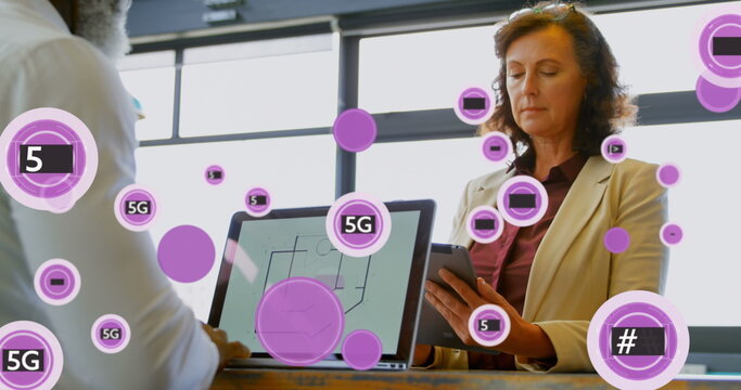 Image of 5g and symbols in circles over diverse coworkers using laptop and digital tablet