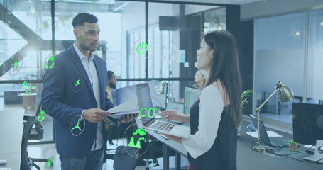 Image of multiple icons over diverse coworkers standing and discussing reports in office