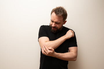 Elbow pain joint problem: middle aged bearded hipster man holds his elbow joint in pain