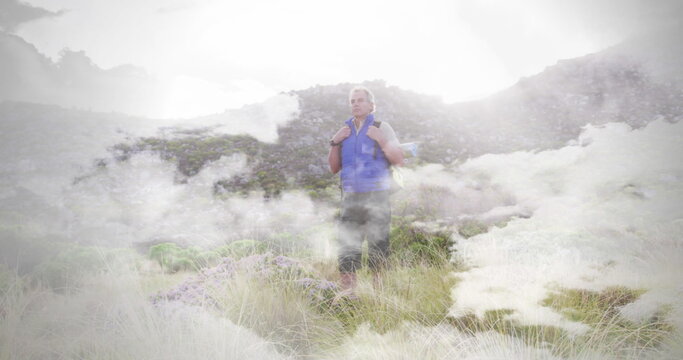 Caucasian senior man hiking standing in countryside, over fast moving clouds