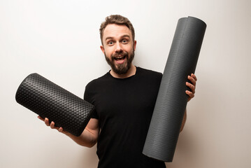 Wellness self care fitness concept: happy bearded hipster holds yoga mat and foam roll
