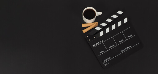 Black Clapper board and hot coffee white cup and two brown sugar sachet  on black background.