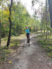 Fototapeta premium A young woman is riding a bicycle in the park and waving her hand. Active recreation in nature