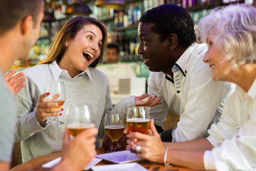 Mixed age range people celebrating holiday together in beer pub, toasting with drinks. Selective...