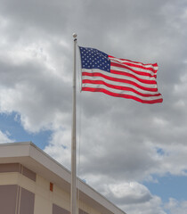 American flag waving in wind in front of building with cloudy sky in background