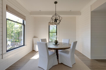 A dining area featuring a sleek table with chairs, accented by a stylish centerpiece. Above, a modern light fixture illuminates the space in a traditional cottage.