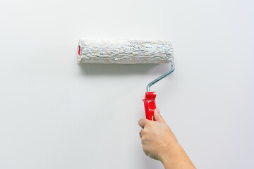 A woman's hand paints a wall white with a paint roller