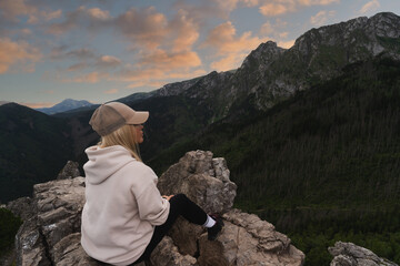 A beautiful girl admires the view at the top of the Polish Tatra Mountains on a summer evening.