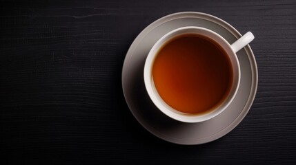 The image shows a white cup of black tea on a gray saucer on the black wooden background. The cup is isolated on the background. The image is suitable for stock agencies.