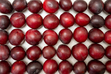 Many red plums stacked in rows on a white background