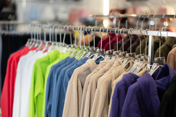 Different hoodies hanging on stand in big clothing store with large assortment