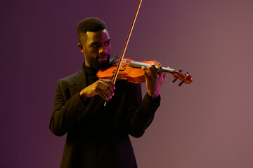 Elegant musician in black suit playing violin against vibrant purple background with skillful...