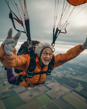 Photo of an elderly retired woman parachuting over some agricultural fields, face of emotion and joy. Active retirement concept