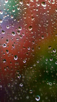 Glass with raindrops. Water drops on window on blurred colorful background. Rain falling outside. Droplets background. Close-up. Vertical video