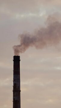 Industrial pipes with smoke against the evening sky. Harmful emissions released from industrial chimney. Air pollution. Vertical video