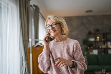 Fototapeta na wymiar One mature blonde woman stand at home use mobile phone talk