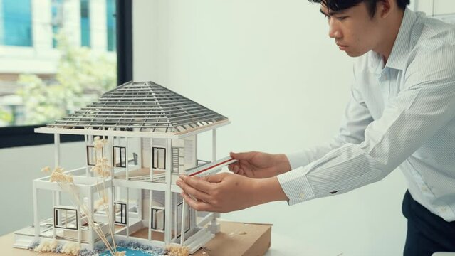 Close up of professional male architect engineer measure house model and using laptop analysis data at meeting table with house model and map . scatter around. Focus on hand. Immaculate.