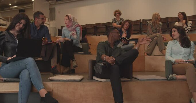 A diverse group of people, encompassing various ages, races, and religions, engage attentively in lectures within the confines of the office learning center, set in an amphitheater-style environment