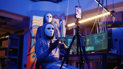 Anonymous evil developers filming ransom video in hidden underground base, threatening to release stolen data publicly if payout demands are not met, using cellphone to record blackmail footage