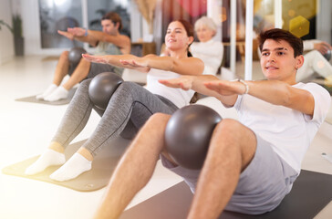 Sporty men and women doing pilates exercises with fitness ball at gym