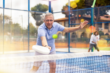 Portrait of emotional aged man enjoying friendly padel tennis match at outdoors court - obrazy, fototapety, plakaty