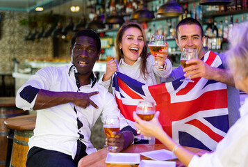 Emotional male and female drinking beer and celebrating success of sports team, waving flag of the...
