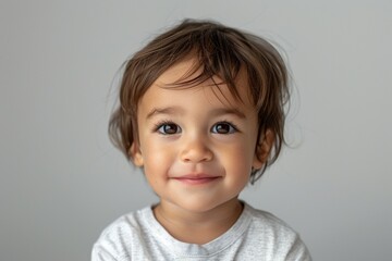 A young child with brown hair and a white shirt is smiling