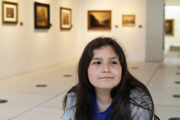 ni&ntilde;o con pelo largo sonriendo sentado en un banco contemplando cuadros en un museo