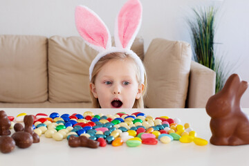 Cute children, kids with rabbit ears hunt looks in surprise at the chocolate eggs on the table