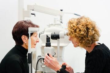 Oculist checking elderly patient's vision using a biomicroscopy machine. Ophtalmology and eyesight concept.