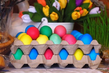Colorful Easter eggs in paper egg box and tulips on background.