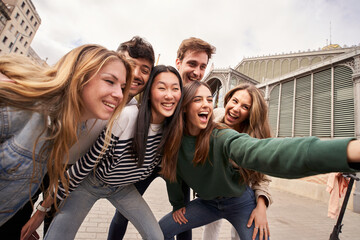 A group of happy young people are smiling and making gestures while taking a selfie together at a...