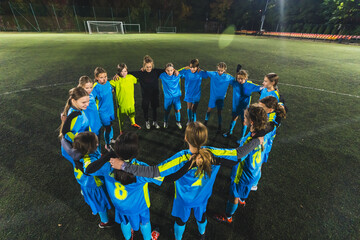 young school girls and their female coach standing in a circle and huddling before starting practice, soccer and teamwork. High quality photo
