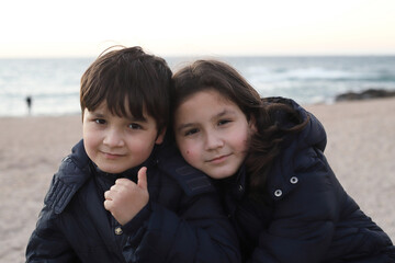 Hermanos abrazados en la playa al atardecer en invierno - 768307828