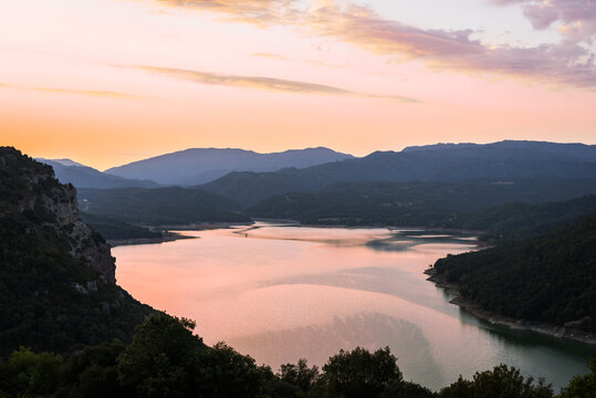 A serene twilight scene, where the setting sun casts a rosy hue over a tranquil lake nestled within the embracing Spanish mountains