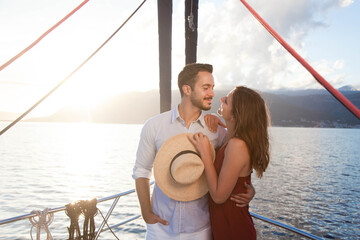 Happy couple in love traveling on yacht at sea. Young travelers smiling and relaxing. Tourists enjoying sunset and summer vacation. Intimate romantic date on sailboat. Journey with beautiful landscape