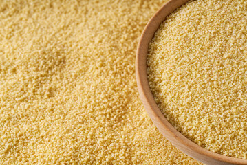Raw couscous are scattered in a wooden bowl close up.