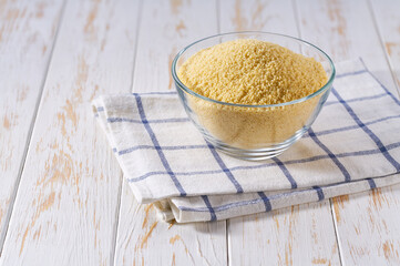Raw couscous in a glass plate on a white wooden table.