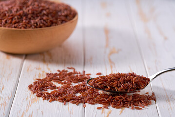 metal spoon with organic red rice on a white wooden table.
