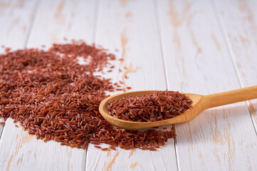 Raw red rice crumble from in a wooden spoon on a white wooden table.